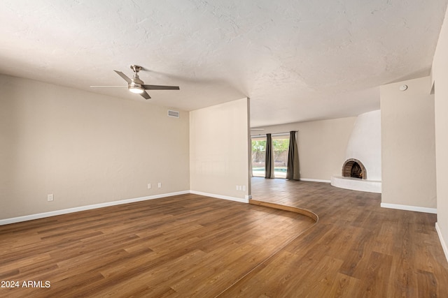 unfurnished living room featuring dark hardwood / wood-style flooring, a textured ceiling, ceiling fan, and a fireplace