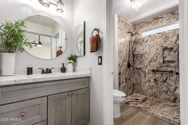 bathroom with vanity, wood finished floors, toilet, walk in shower, and a ceiling fan