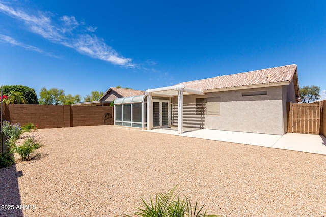 rear view of property with a fenced backyard, a sunroom, a patio area, and a tile roof