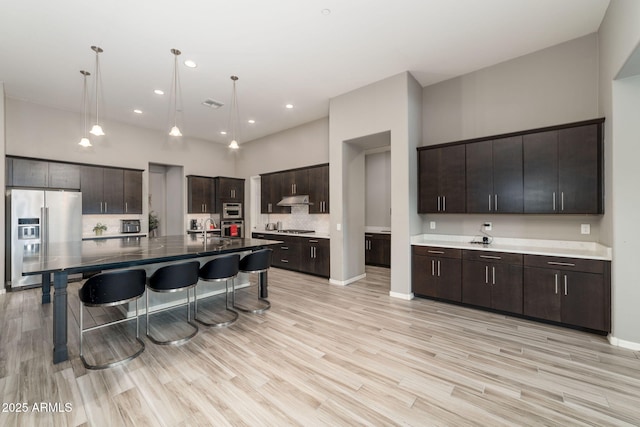 kitchen with a kitchen island with sink, hanging light fixtures, dark brown cabinetry, and appliances with stainless steel finishes