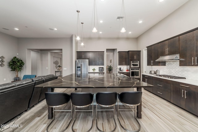 kitchen featuring a kitchen island with sink, pendant lighting, dark brown cabinets, and appliances with stainless steel finishes