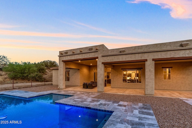 back house at dusk with a fenced in pool and a patio