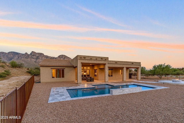 pool at dusk with a hot tub, a mountain view, and a patio