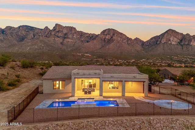 back house at dusk featuring a patio, a mountain view, and a pool with hot tub