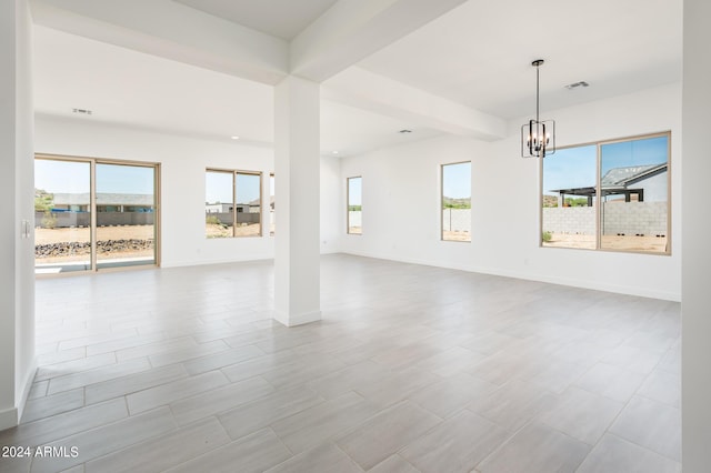 empty room with baseboards, beam ceiling, a notable chandelier, and plenty of natural light