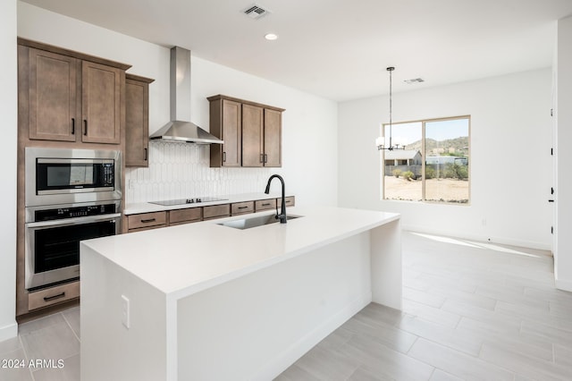 kitchen with visible vents, a sink, stainless steel appliances, wall chimney exhaust hood, and tasteful backsplash