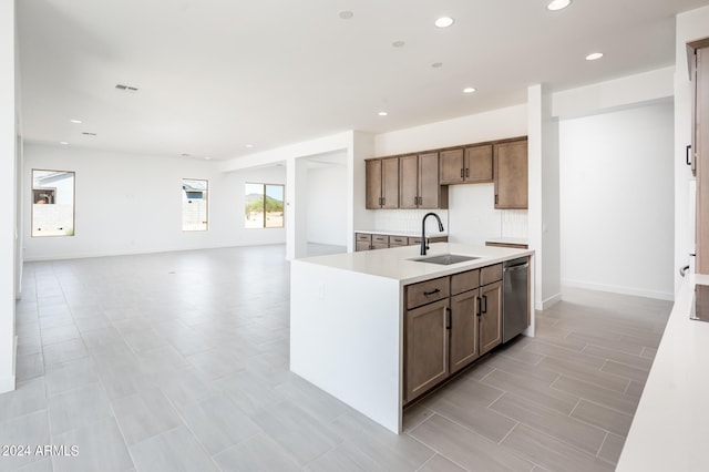 kitchen featuring a center island with sink, a sink, light countertops, stainless steel dishwasher, and backsplash