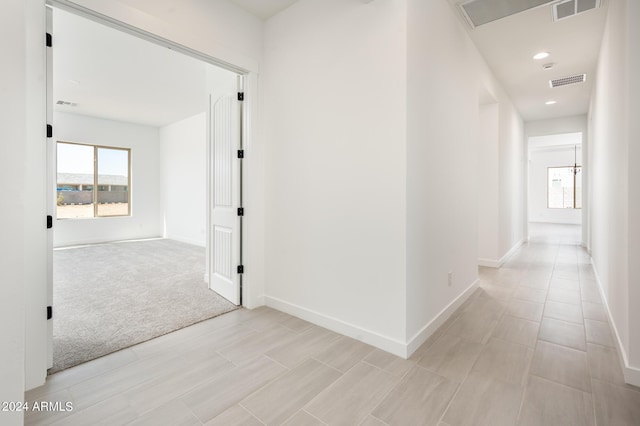 hallway with a wealth of natural light, visible vents, and light colored carpet