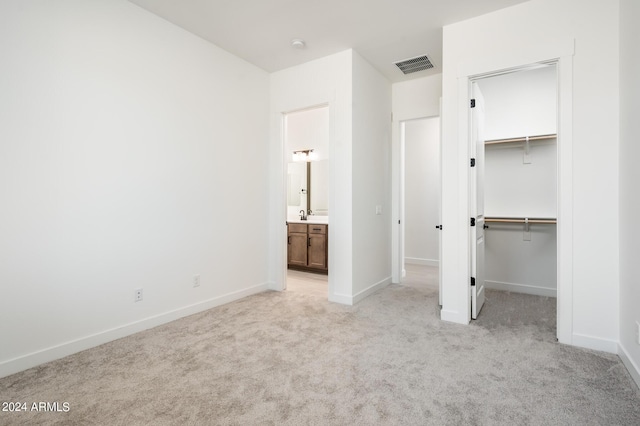 unfurnished bedroom featuring a spacious closet, baseboards, visible vents, and light carpet