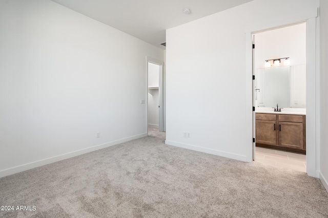 unfurnished bedroom with light carpet, ensuite bathroom, a sink, baseboards, and a spacious closet