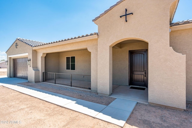 doorway to property with stucco siding, a garage, and a tile roof