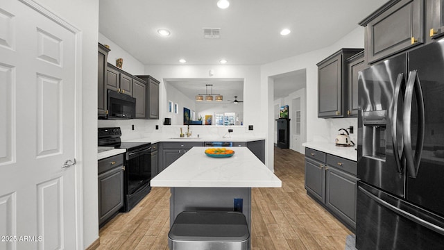 kitchen featuring black appliances, recessed lighting, a kitchen island, and light wood-style floors