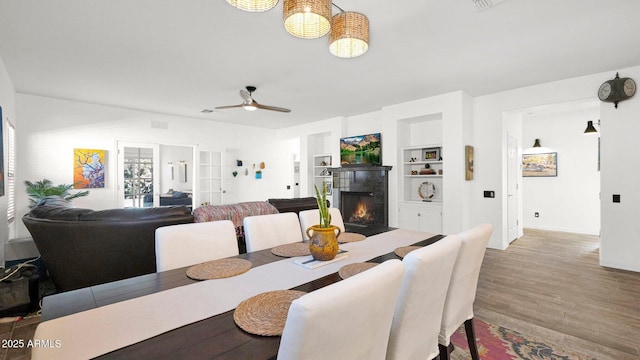 dining area featuring baseboards, ceiling fan, wood finished floors, built in shelves, and a fireplace