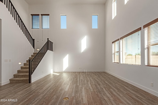 unfurnished living room with hardwood / wood-style floors and a towering ceiling