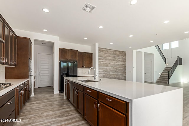 kitchen with black fridge, a center island with sink, sink, dark brown cabinetry, and light wood-type flooring