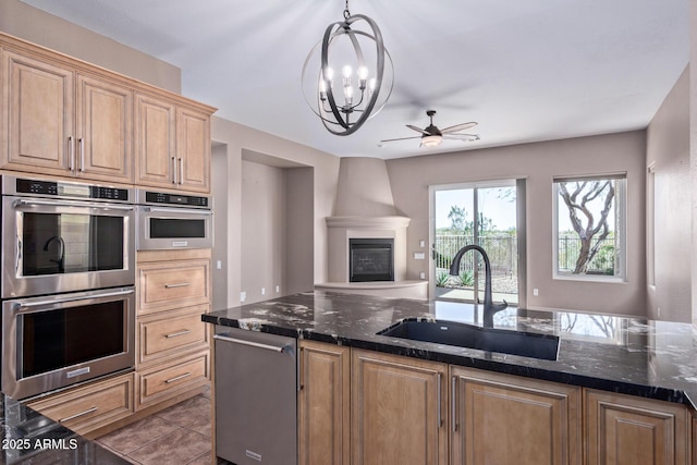 kitchen with a fireplace, a sink, appliances with stainless steel finishes, dark stone counters, and decorative light fixtures