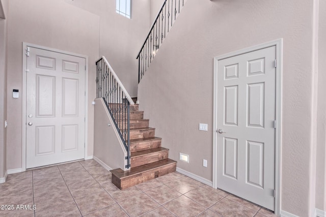 entrance foyer featuring light tile patterned floors, stairway, a towering ceiling, and baseboards