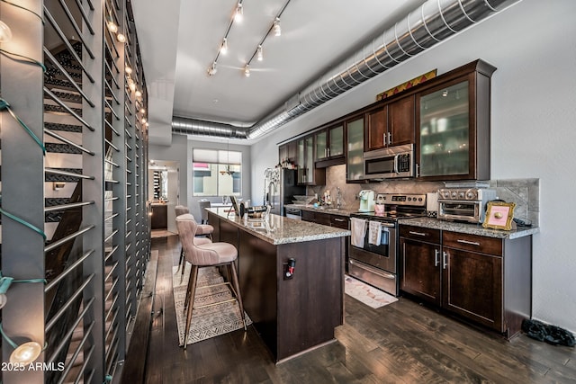 kitchen featuring a breakfast bar area, stainless steel appliances, light stone counters, a center island with sink, and decorative backsplash