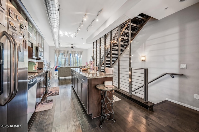 kitchen with dark brown cabinets, a kitchen breakfast bar, stainless steel appliances, a center island, and dark hardwood / wood-style flooring