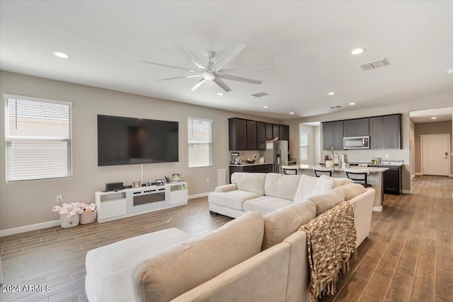 living room featuring visible vents, baseboards, a ceiling fan, and wood finished floors