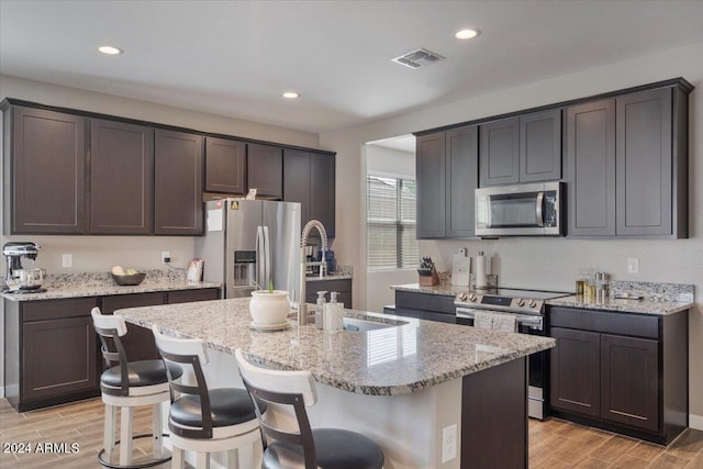 kitchen featuring stainless steel appliances, visible vents, light stone counters, and wood finish floors