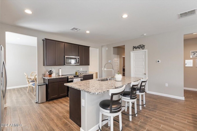 kitchen with light hardwood / wood-style floors, a center island with sink, sink, stainless steel appliances, and light stone countertops