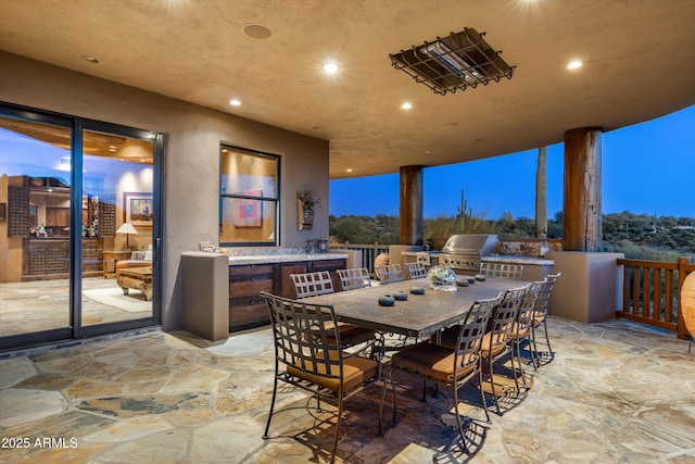 patio terrace at dusk featuring a bar, area for grilling, and exterior kitchen