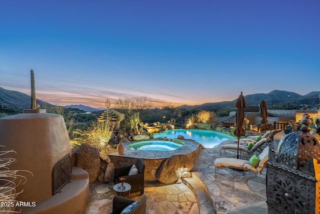 pool at dusk with an in ground hot tub, a mountain view, and a patio area