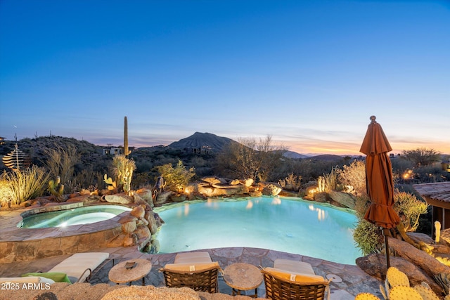 pool at dusk featuring a mountain view and an in ground hot tub