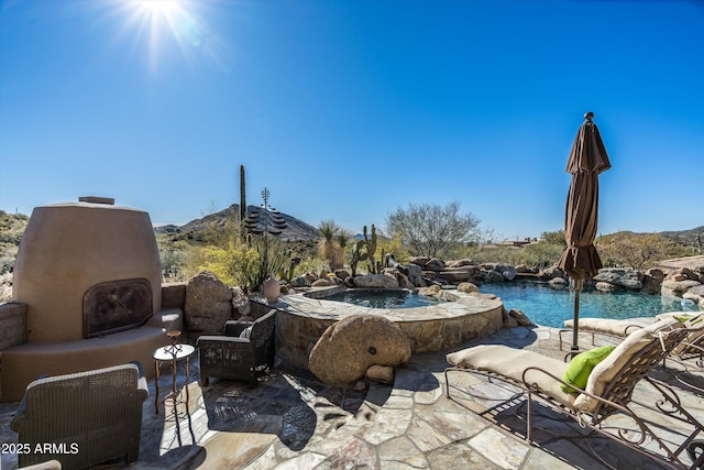 view of patio featuring an outdoor fireplace and a swimming pool with hot tub