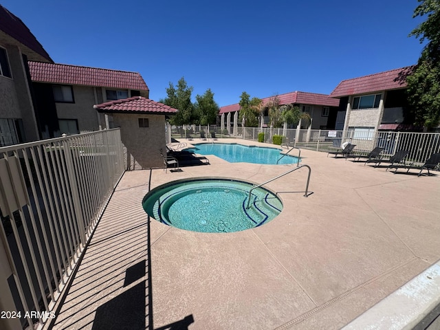 community pool with fence, a patio area, and a hot tub