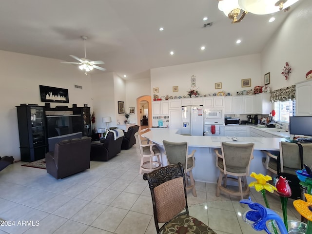 kitchen with white appliances, ceiling fan, light tile patterned floors, a high ceiling, and white cabinetry