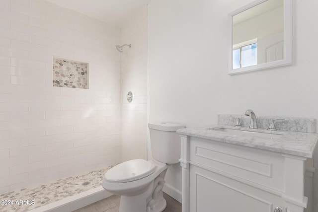 bathroom with toilet, tile patterned floors, tiled shower, and vanity