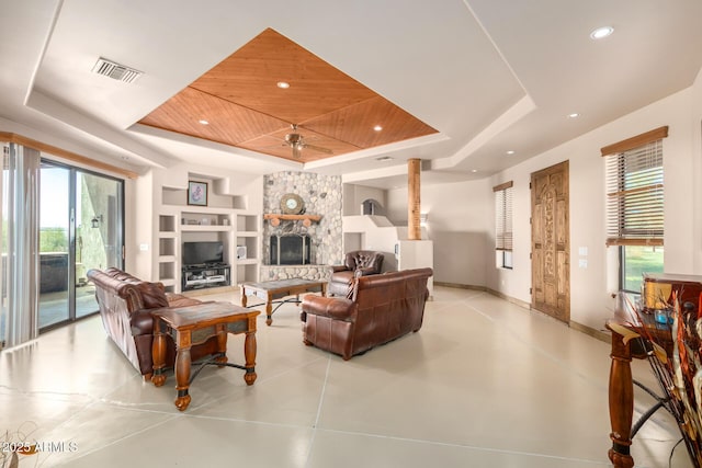 living room featuring a raised ceiling, a stone fireplace, ceiling fan, and built in shelves