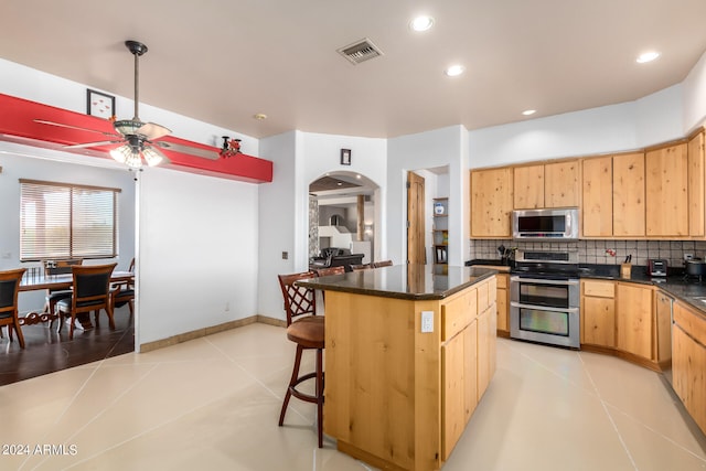 kitchen with ceiling fan, appliances with stainless steel finishes, backsplash, a kitchen island, and light brown cabinets