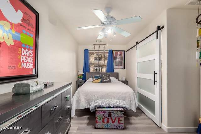 bedroom featuring visible vents, a ceiling fan, a barn door, and wood finished floors