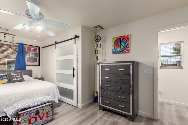 bedroom featuring visible vents, light wood-style flooring, baseboards, and a barn door