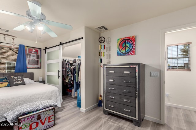 bedroom with visible vents, a walk in closet, a barn door, light wood-style floors, and a closet