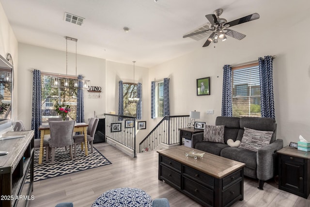 living area with visible vents, light wood-style flooring, and ceiling fan with notable chandelier