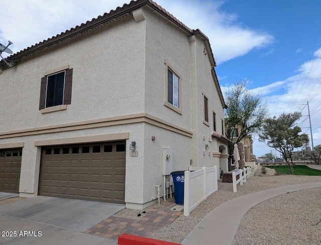 view of side of property with concrete driveway, a tiled roof, a garage, and stucco siding