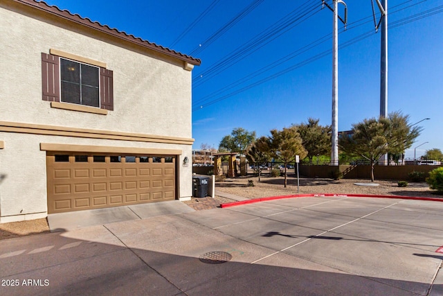 exterior space featuring fence, a tile roof, stucco siding, driveway, and an attached garage