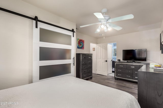 bedroom featuring ceiling fan, a barn door, and dark wood-style flooring