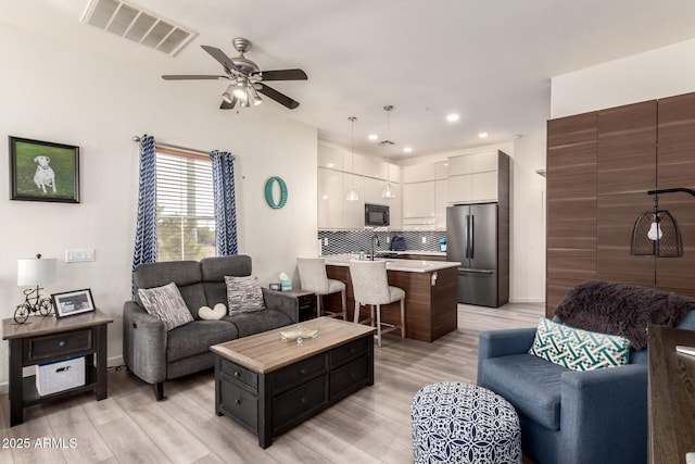 living room featuring light wood finished floors, visible vents, baseboards, and ceiling fan