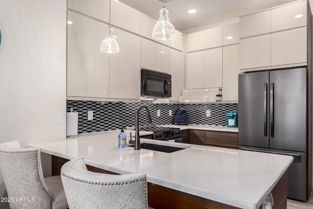 kitchen with a peninsula, modern cabinets, freestanding refrigerator, and black microwave