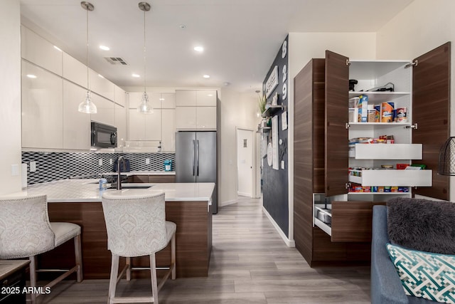 kitchen with visible vents, a peninsula, stainless steel refrigerator, black microwave, and modern cabinets