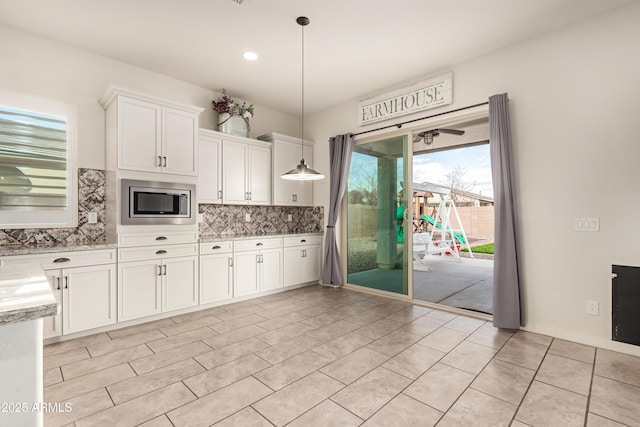 kitchen with stainless steel microwave, pendant lighting, white cabinets, and tasteful backsplash