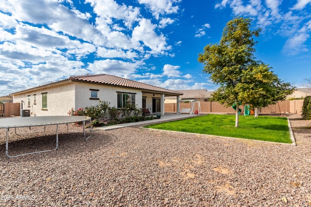 back of property with a trampoline and a yard