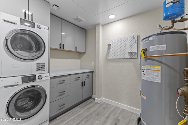 laundry area featuring cabinets, stacked washer / dryer, water heater, and light wood-type flooring