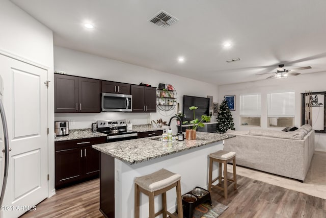 kitchen featuring a breakfast bar, a center island with sink, light hardwood / wood-style flooring, dark brown cabinets, and stainless steel appliances