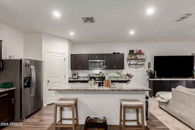 kitchen featuring a kitchen bar, stainless steel appliances, an island with sink, and light hardwood / wood-style flooring